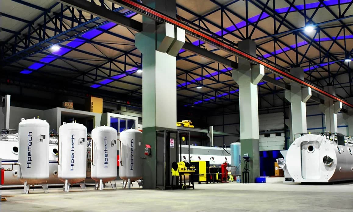 Hipertech factory interior under blue accent lighting, rows of cylindrical vessels between structural columns