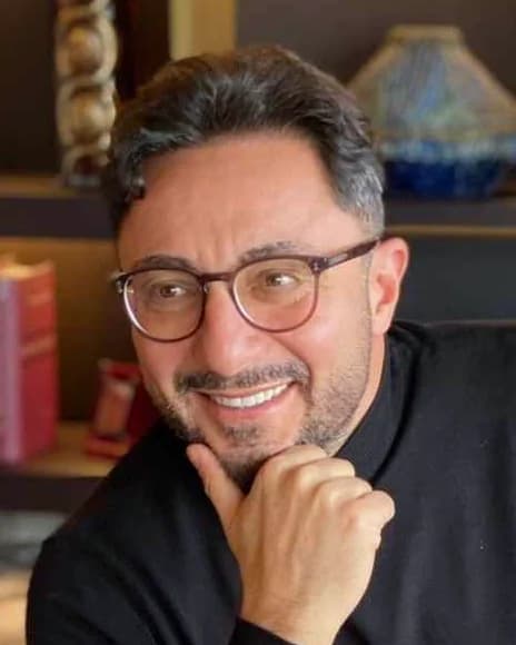 Op. Dr. Aytunç Yur, in a black roll-neck and glasses, chin resting on his hand