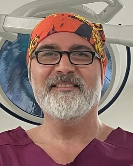 Prof. Dr. Ender İnci, in surgical scrubs and cap, an operating-theatre light behind him