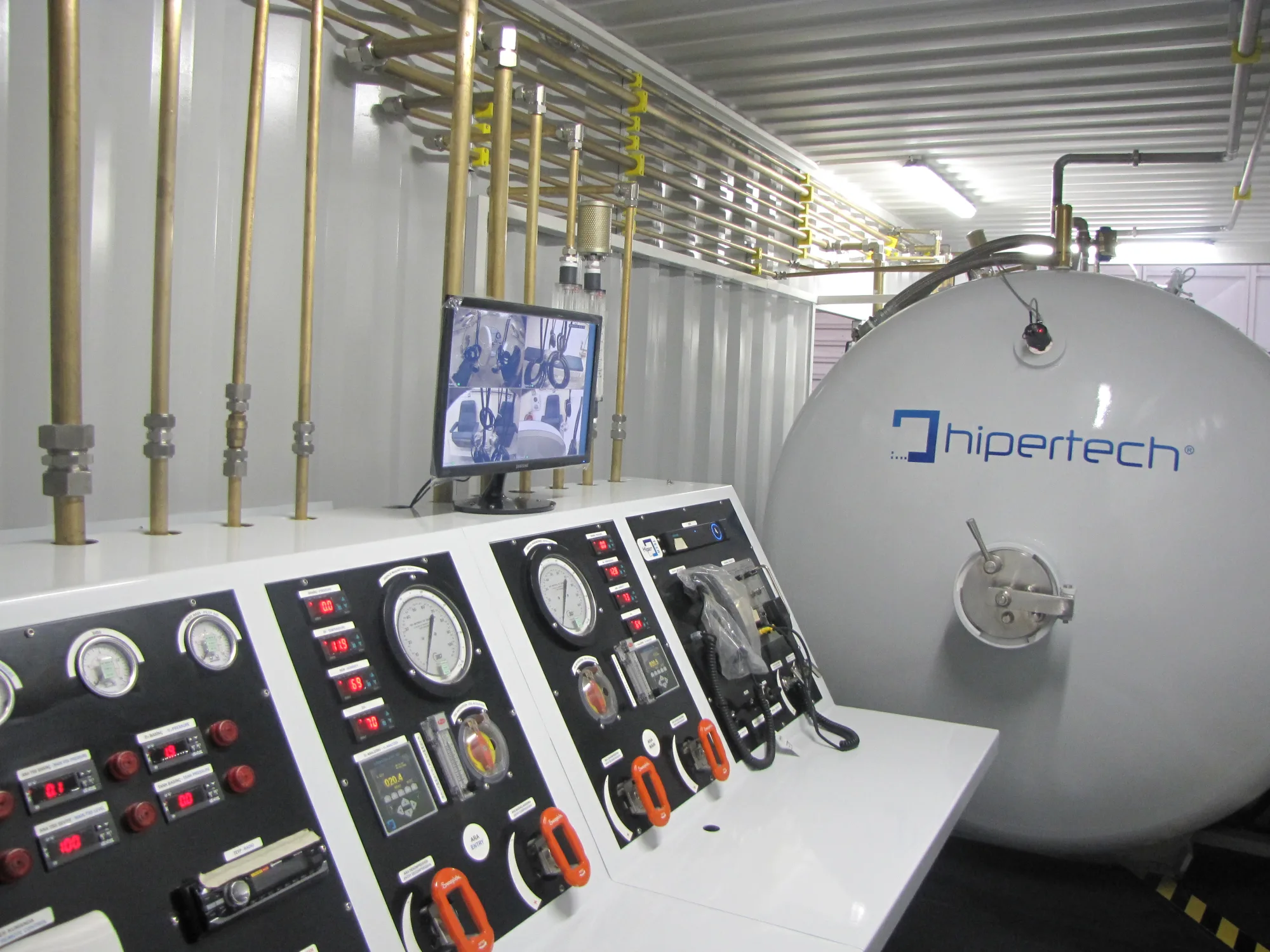 Inside an open containerized system: the white chamber with its hipertech decal and the control console in front of it, under the container roof