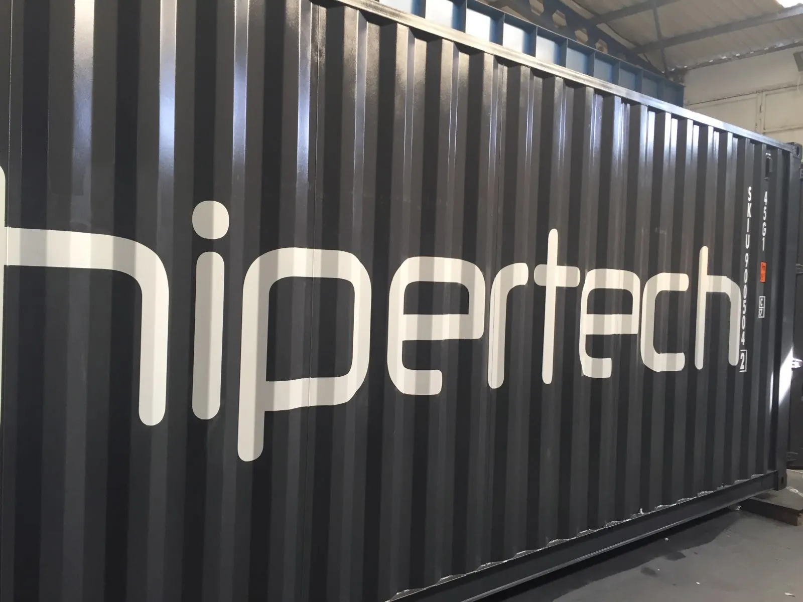 The grey wall of a Hipertech containerized chamber, the Hipertech wordmark running its full height