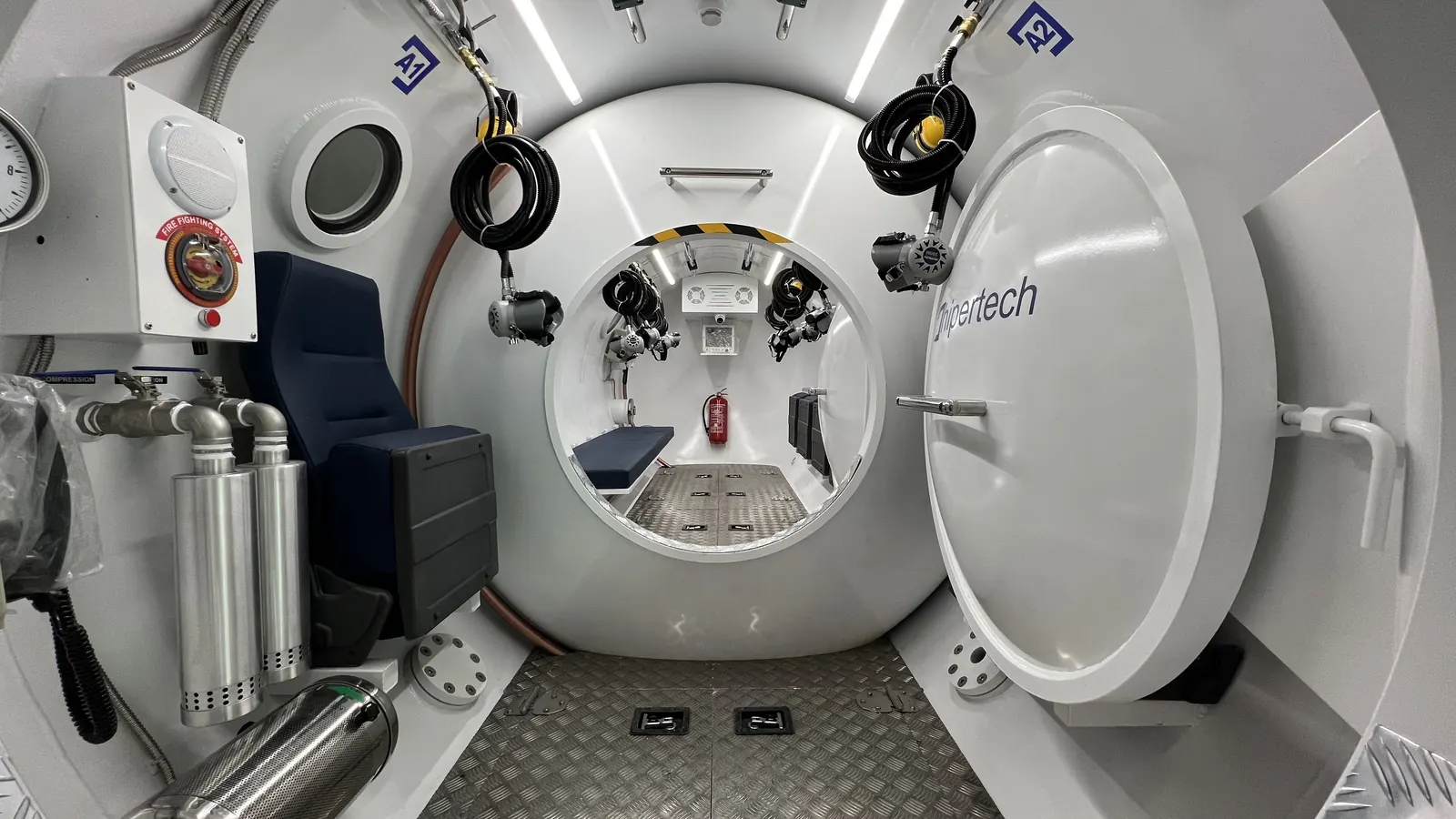 Inside a twin-lock decompression chamber: a seat and cylinder rack in the near lock, the inner door open on the far lock, the outer door swung clear