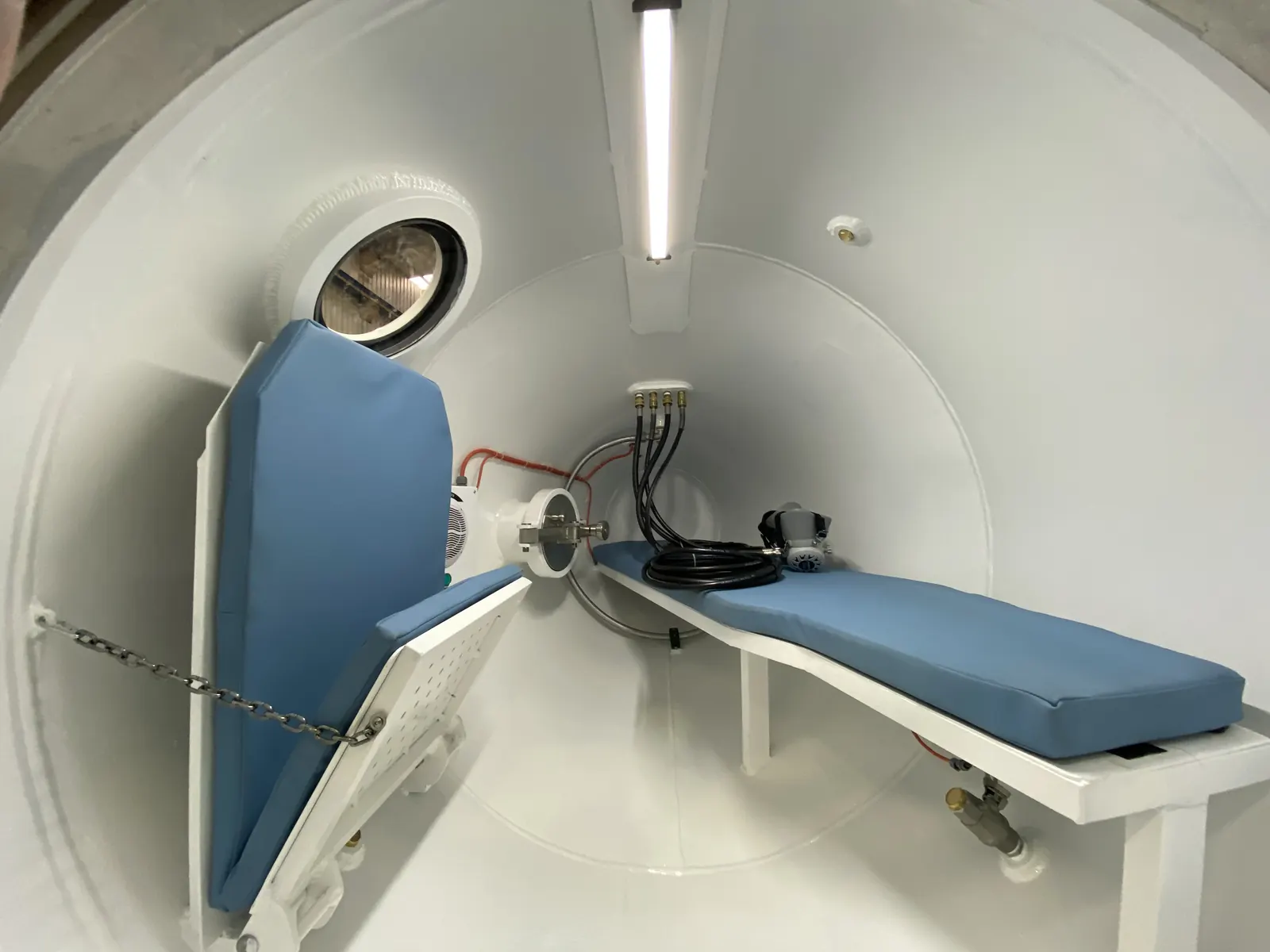 Inside a transportable recompression chamber: a padded bench the length of the hull, a fold-down seat, overhead gas ports and a mask on its hose