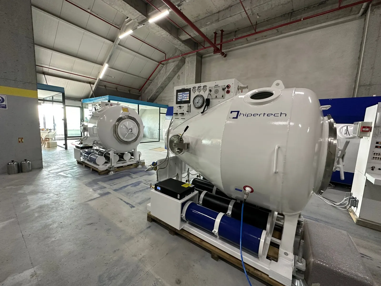 A transportable recompression chamber on its white skid with composite cylinders mounted under the frame, in a warehouse