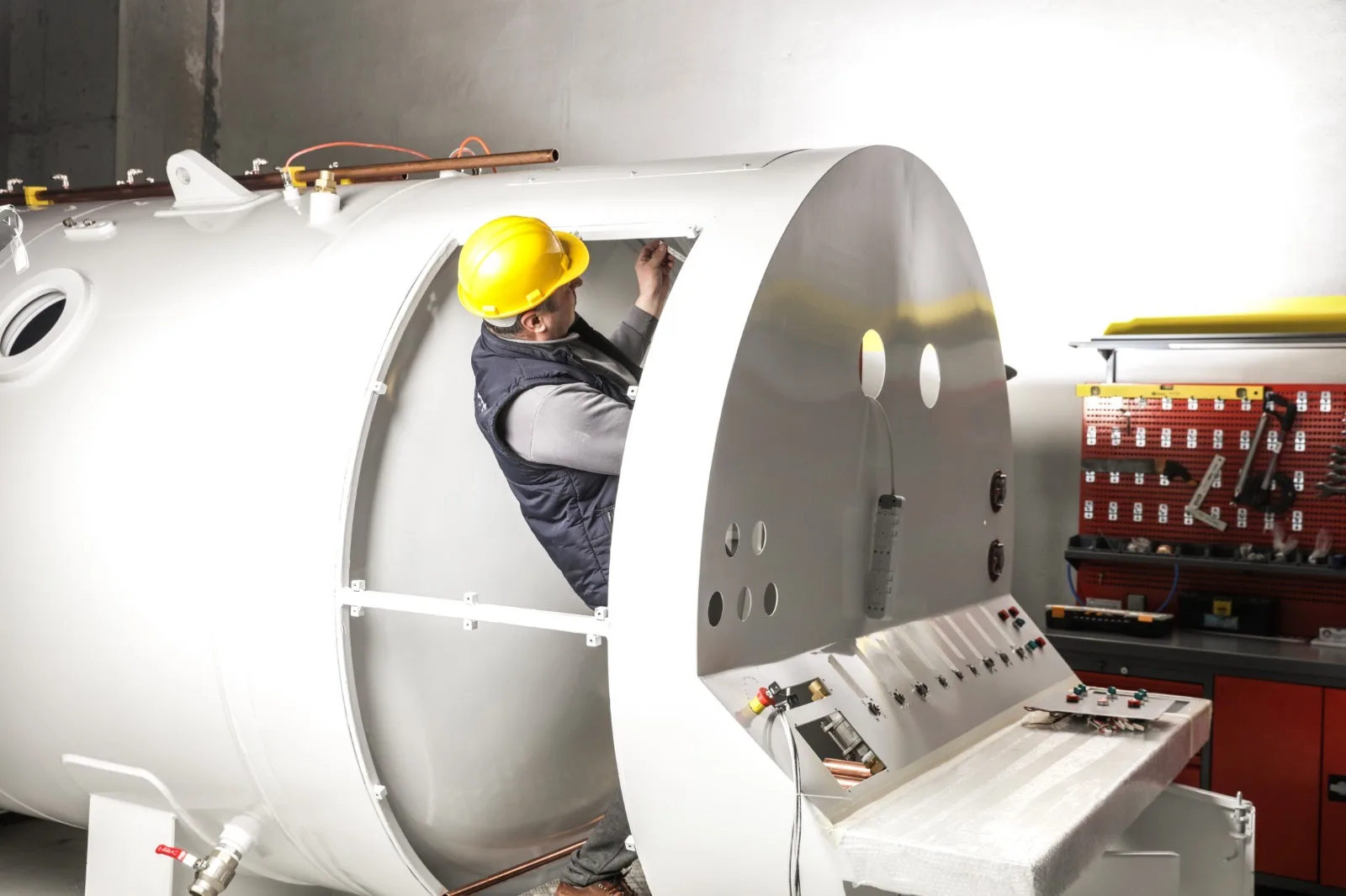 A Hipertech technician in a hard hat fitting the porthole door hinge assembly of a chamber