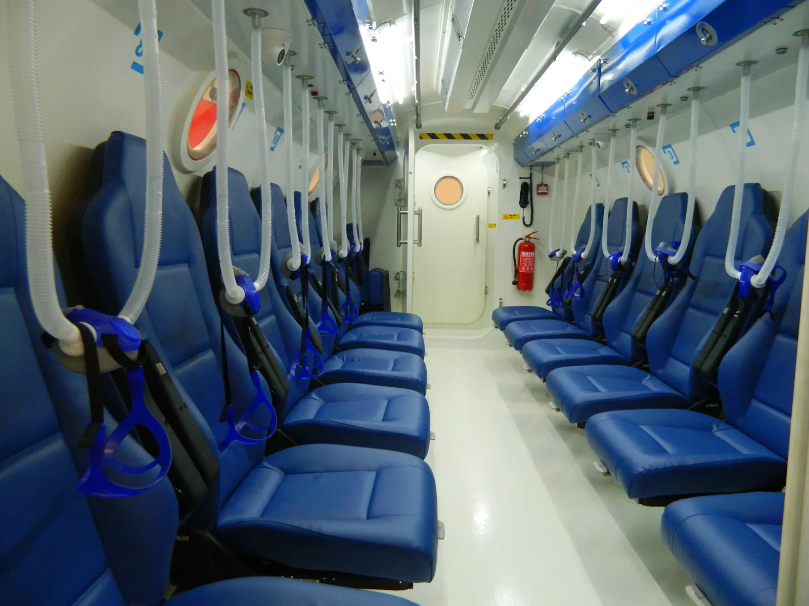 Inside a Multiplace Omega: two rows of seats down the aisle, a breathing hose and a head harness at each seat