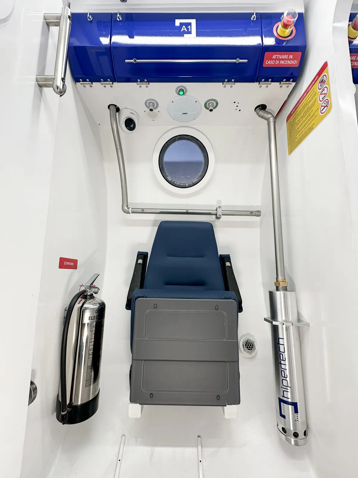 Inside the lock of a Multiplace Omega: a stowed patient trolley, a fire extinguisher, a hand-line and a round viewport in the door