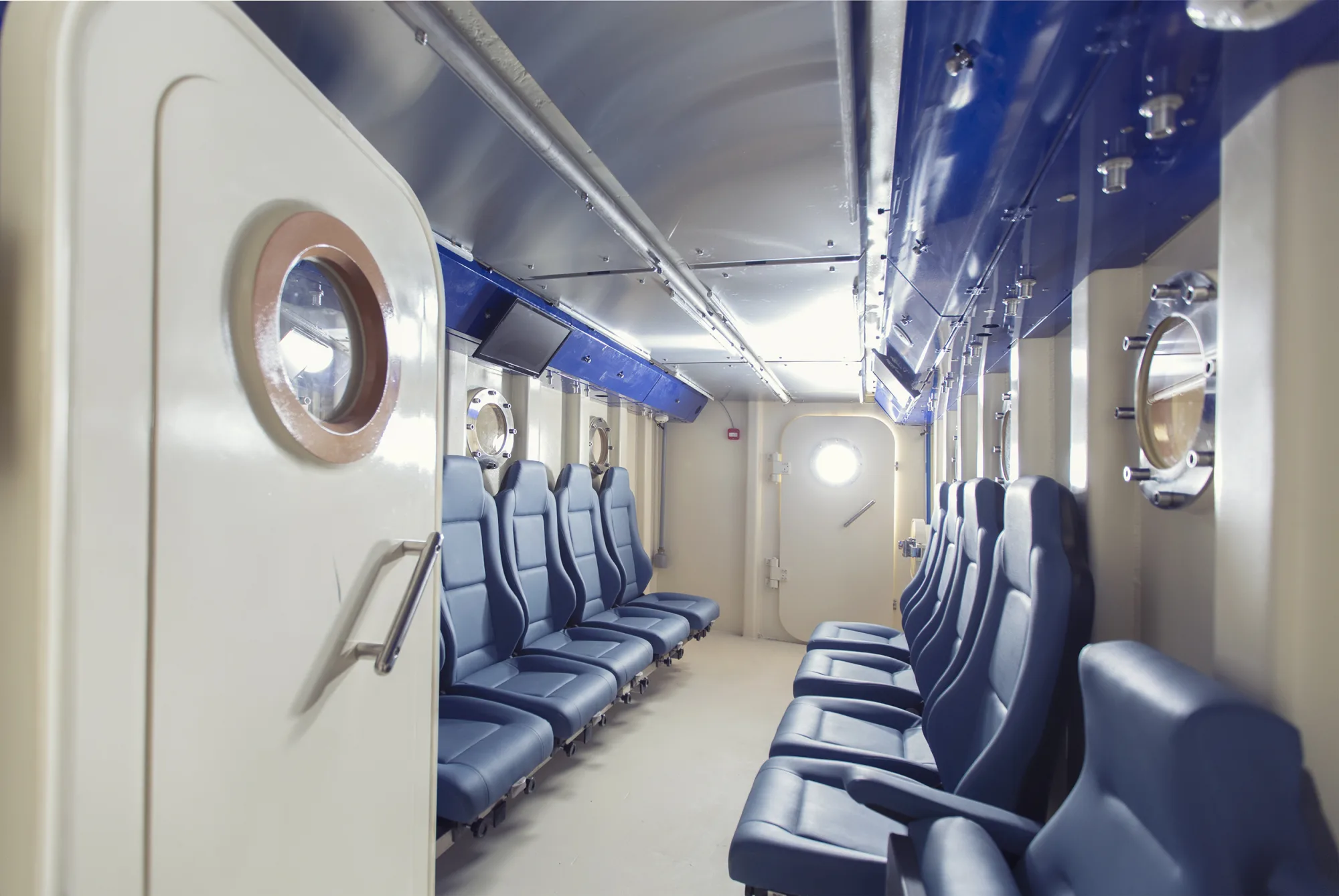 The interior aisle of a Multiplace Quadro, seats either side, porthole windows and ceiling grab rails